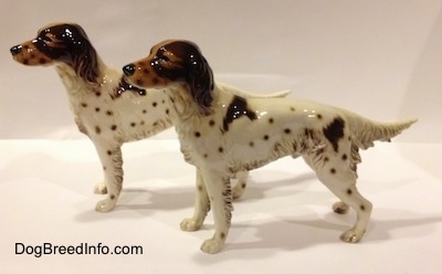 The left side of two porcelain brown and white English Setter figurine. The figurines brown faces and black circles for eyes.