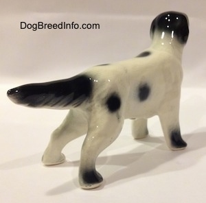 The back right side of a white and black ceramic English Setter figurine in a standing pose. The figurine has long legs and short paws.