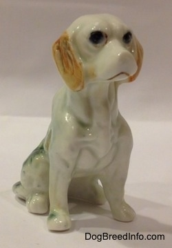 The front right side of an English Setter in a sitting pose figurine. The figurine has big black circles for eyes.