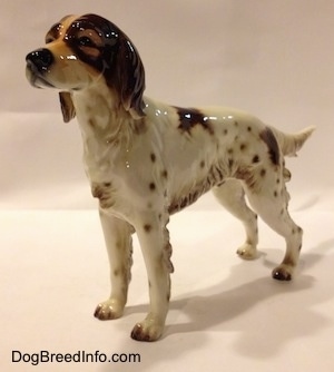 The front left side of a figurine of a brown and white porcelain English Setter. The figurine has a detailed brown face.