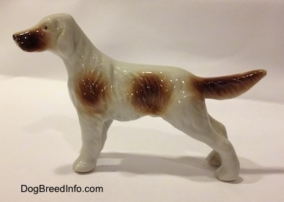 The left side of a white and brown bone china English Setter figurine. The figurine has a brown muzzle and a brown tail.