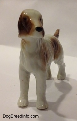 A brown and white bone china English Setter figurine in a standing pose has black circles for eyes.