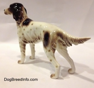 The back left side of a white with brown Rnglish Setter figurine in a standing pose. The figurine has a long body and around the trim of its body and legs are hair details.