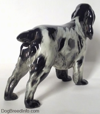 The back right side of a black and white English Springer Spaniel figurine. The figurine has a short black tail and it is level with its body.