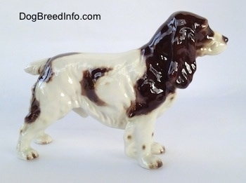 The right side of a figurine of a white with brown English Springer Spaniel figurine. The figurine has hair all along the edge of its body and legs.