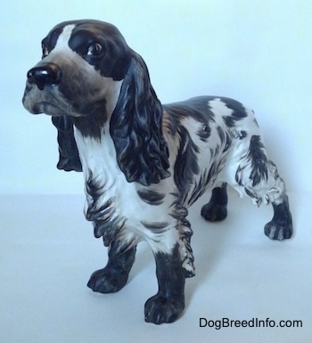 The front left side of a figurine of a English Springer Spaniel with a matte finish. The figurine has large black and bushy ears.