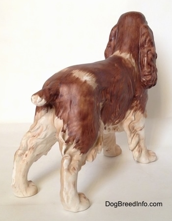 The back right side of a brown and white English Springer Spaniel figurine in a standing pose with a matte finish. The figurine has a short brown tail.