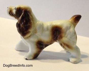 The left side of a figurine of a brown and white English Springer Spaniel figurine. The figurine has a short brown tail and it has large brown ears.