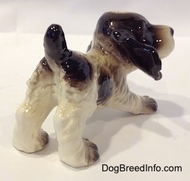 The back right side of an English Springer Spaniel puppy in a play bow pose figurine. The ears of the figurine are big and liver colored.