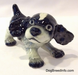 The front right side of a figurine of a black and white English Springer Spaniel puppy in a play bow pose. The figurine has its ears sticking out.