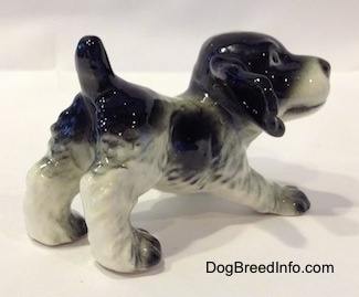 The back right side of a black and white English Springer Spaniel puppy in a play bow pose figurine. The figurine looks like it has ruffled hair on it.
