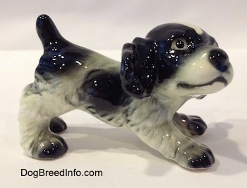 The right side of a black and white English Springer Spaniel puppy in a play bow pose figurine. The figurine has black spots along its side.