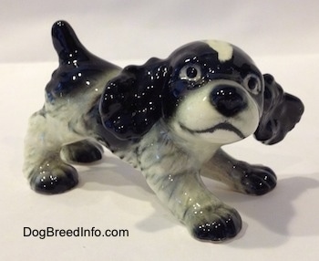 A black and white English Springer Spaniel puppy in a play bow pose figurine. The figurine has black circles for eyes.