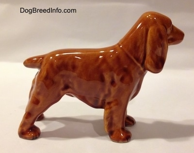 The right side of a ceramic brown Field Spaniel figurine. The figurine has a short brown tail that is up and level with the body.