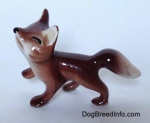 The left side of a Baby Fox figurine that is looking up, it has black lines for eyes and a black circle for its nose.