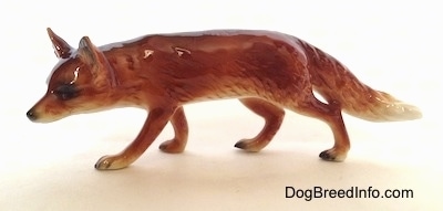 The left side of a red fox figurine that is in a stalking pose. The figurine has black nails at the tips of its paws, a long tail that it is carrying low, a long pointy snout and perk ears.