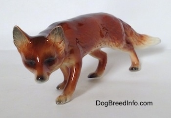 The front left side of a red Fox figurine in a stalking pose. The figurine has black eyes and a black nose and perk ears that stick up to a point.
