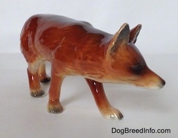 The front right side of a red fox figurine in a stalking pose. The ears of the figurine are standing up in the air.