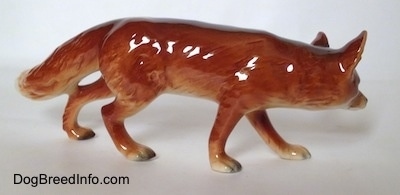 The right side of a red fox figurine in a stalking pose. The figurine has a long body and short legs.