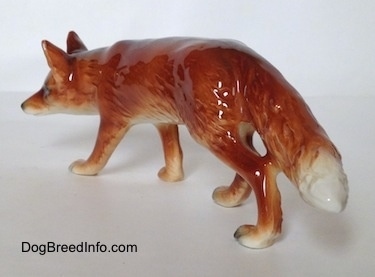 The back left side of a red fox figurine in a stalking pose. The figurine is glossy.