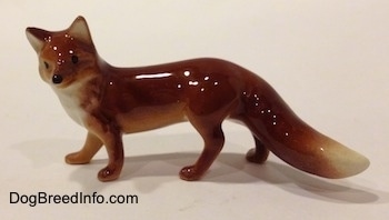 The left side of a red fox figurine. The figurine has black circles for eyes and it has a black circle for a nose.