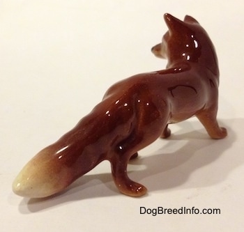 The back right side of a figurine of a red fox. The figurine has a red tail with a white tip.