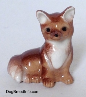 A figurine of a baby Fox that is seated. The figurine ahs black circles for eyes and a nose.