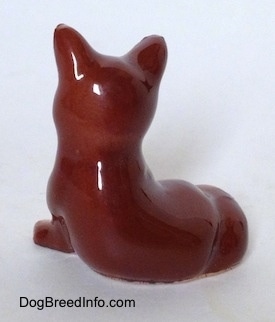 The back of a figurine of a baby fox that is seated. The figurine is glossy.