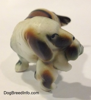 A brown and white with black bone china of a French Brittany Spaniel carrying a puppy. The figurine has a black dot for a nose.