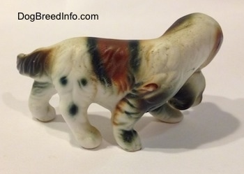 The right side of a brown and white with black bone china of a French Brittany Spaniel carrying a puppy. The figurine has fine hair details.