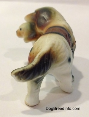 The back of a brown and white with black bone china of a French Brittany Spaniel carrying a puppy. The figurine has a long tail.