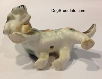 The underside of a bone china of a French Brittany Spaniel carrying a puppy. There is a hole on the underside of the figurine.