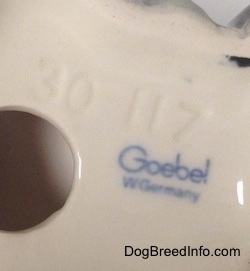 Close up - The underside of a French Bull Tzu with a hole in the bottom of the figurine. To the right of the hole is the stamped text logo of a Goebel W.Germany and above the hole is the engraved numbers - 30 117.