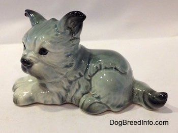 The left side of a white with black French Bull Tzu figurine in a laying down pose. The figurine has a detailed face and black circles for eyes.
