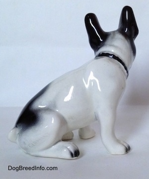 The right side of a white and black French Bulldog that is sitting figurine. The figurine has short legs and small paws.