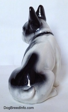 The back right side of a white and black figurine of a French Bulldog that is sitting. The figurine has large black ears.