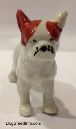 A white with red bone china French Bulldog figurine that has black circles for eyes.