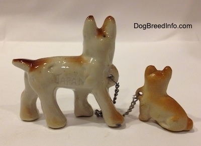 The left side of a brown with white and black French Bulldog that has the word - JAPAN - engraved on it. The figurine is also chained to a figurine of a brown with tan Frenchie puppy.