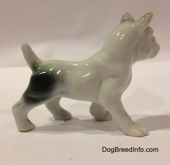 The right side of a white with brown and green French Bulldog porcelain figurine in a standing pose. The figurine has a large green spot on its hind leg.