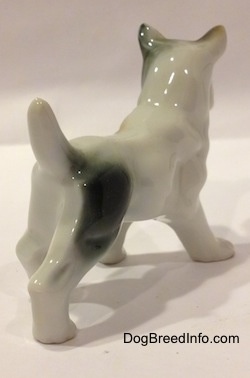 The back right side of a porcelain figurine white with brown and green French Bulldog in a standing pose. The figurine is very glossy.