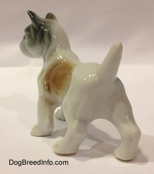 The back left side of a white with brown and green French Bulldog porcelain figurine that is in a standing pose. The figurine has a brown spot on its left side.