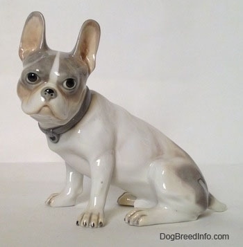 The left side of a white with grey French Bulldog. The Bulldog figurine has a detailed face and large standing ears.