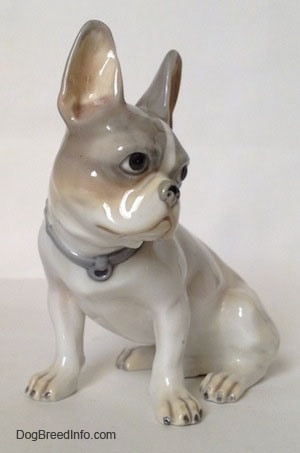 A figurine of a white with grey French Bulldog that has white paws with black nails.