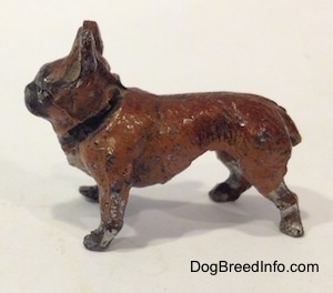 The left side of a brown with black French Bulldog figurine made of metal. The figurine has a short tail and big standing ears.