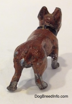 The back right side of a brown with black French Bulldog metal figurine. The figurine has a short body with chips all over it.