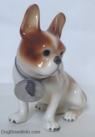A brown and white French Bulldog in a sitting pose figurine. The figurine has large brown ears in the air.