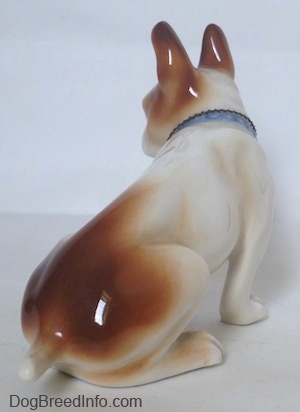 The back right side of a brown and white French Bulldog figurine. The bottom and tail end of a figurine is brown. The figurine has a short tail.