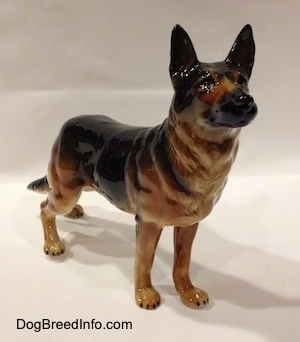 The front right side of a figurine of a black and tan German Shepherd standing. The figurine has detailed black circles for eyes and a black muzzle.