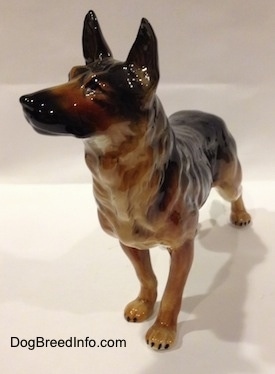 The front left side of a black and tan German Shepherd standing figurine. The figurine has long legs with black tipped nails.