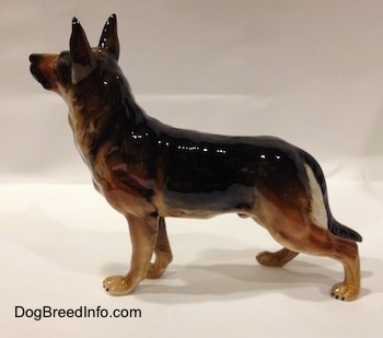 The left side of a figurine of a black and tan standing German Shepherd. The figurine is glossy.